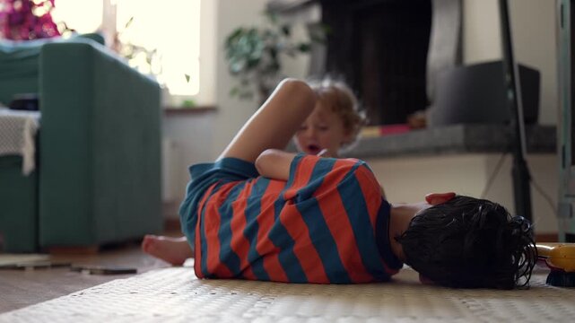 Toddler and sibling playing with toy on floor, smiling and engaged in shared activity during relaxed home setting