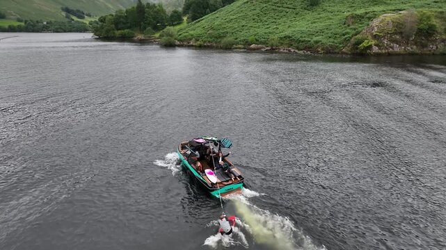 Aerial orbit tracking boat and wake surfer falling with Ullswater mountains in view Lake District UK