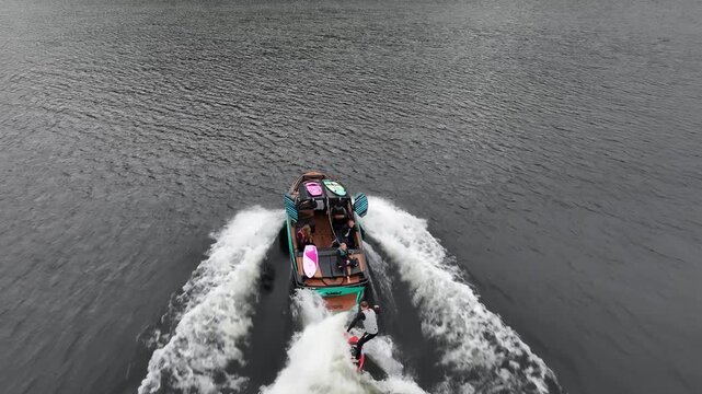 Aerial tracking shot of wake surfer carving on Ullswater lake wave falling at end Lake District UK cloudy day
