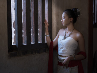 Beautiful, pretty young Asian woman wearing traditional Thai dress, Lanna style, standing beside an...