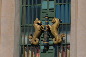 Two ornate golden sea-horse sculptures with coiled tails are mounted on a decorative dark pole,...