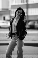 Portrait of a young beautiful long-haired girl in a black jacket outdoors. Black and white photo.