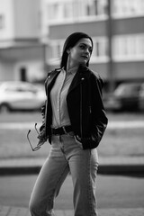 Portrait of a young beautiful long-haired girl in a black jacket outdoors. Black and white photo.