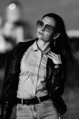 Portrait of a young beautiful long-haired girl in a black jacket outdoors. Black and white photo.