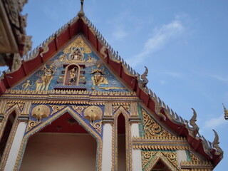 Fototapeta premium Intricate multi-tiered roof of a traditional Thai temple, with vibrant colors and ornate finials against a clear blue sky. Highlights cultural architecture.