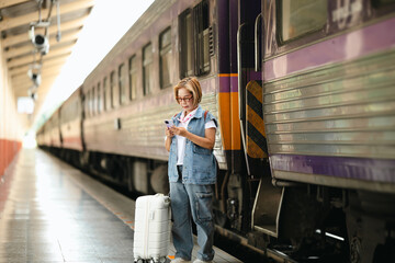 Mature female traveler using smartphone at train platform