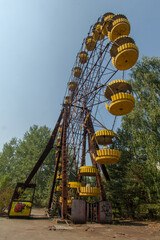 Abandoned Ferris Wheel with Yellow Cabins in Overgrown Park under Clear Blue Sky in Prypjat,...