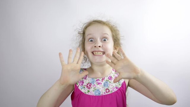 A cute girl smiles, looks at the camera, waves her hands in greeting. Expressive emotion.