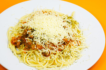 A generous serving of spaghetti bolognese topped with a mound of shredded cheese and herbs.