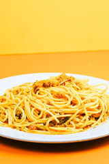 A classic plate of spaghetti with a rich, savory meat sauce, served on a white dish against an orange background.
