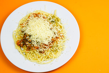 A generous serving of spaghetti bolognese topped with a mound of shredded cheese and herbs.