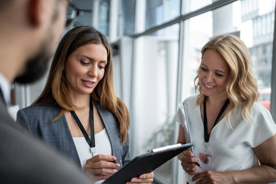 Businesswomen wearing lanyard showing clipboard to businessman at conference