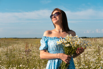 Young woman smiling while smelling daisies in field. Concept of peace and contentment. Summer bliss forever captured in this frame.