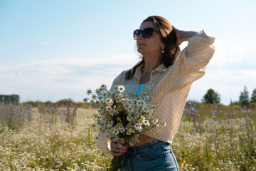Young woman smiling while smelling daisies in field. Concept of peace and contentment. Summer bliss forever captured in this frame.