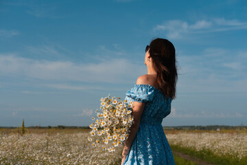 Young woman smiling while smelling daisies in field. Concept of peace and contentment. Summer bliss forever captured in this frame.