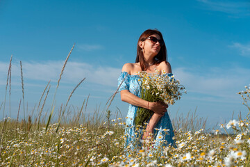 Young woman smiling while smelling daisies in field. Concept of peace and contentment. Summer bliss forever captured in this frame.