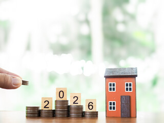 Miniature house, Wooden blocks with number 2026 on stack of coins. The concept of saving money for...