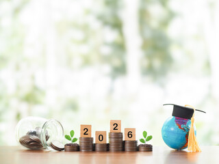 Earth globe with graduation hat, Wooden block with number 2026 and plant growing on stack of coins....