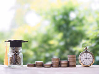 Glass bottle with graduation hat, Vintage watch and stack of coins. The concept of saving money and manage time for education, student loan, scholarship, tuition fees