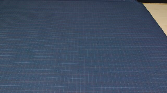female unrolling roll  blue fabric on cutting table at sewing factory