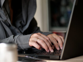 Close-up of Hooded Figure's Hands Typing on Laptop Keyboard, Focused Digital Work.