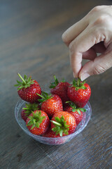 Hands are picking strawberries. Many fresh strawberries in a clear plastic glass lid on a wooden table background, fruit, food, decor, object, copy space