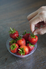 closeup hands are picking strawberries. Many fresh strawberries in a clear plastic glass lid on a wooden table background, fruit, food, decor, object, copy space