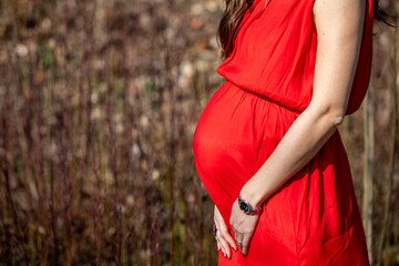 Beautiful pregnant woman feeling happy in nature while taking care of her child. Young expecting mother holding baby in pregnant belly. Maternity prenatal care and woman pregnancy concept.