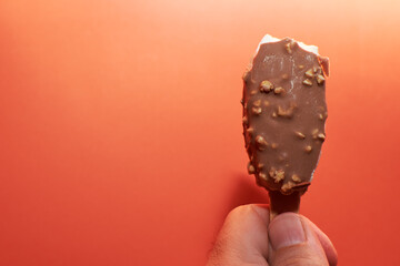 Chocolate ice cream on a stick against orange background.