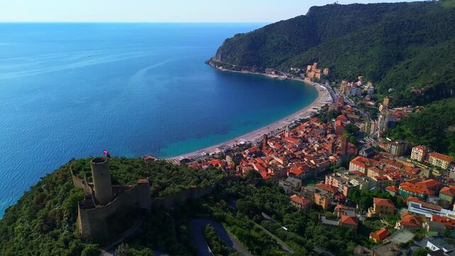 Aerial view of the Ancient Castle of Monte Ursino, on top of a hill, ancient elements and buildings of the original settlement of Noli. fpv. Red flag with a cross on the towers. Noli Italy 01.09.2025
