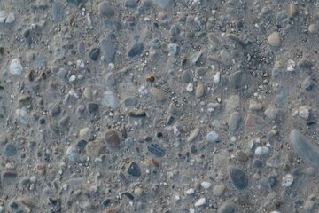 Pebble-embedded grey surface texture showcasing various rock fragments and sand particles creating