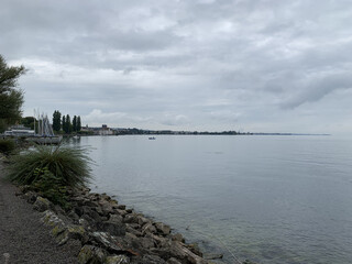 Overcast day by a calm lakeside with distant town and boats