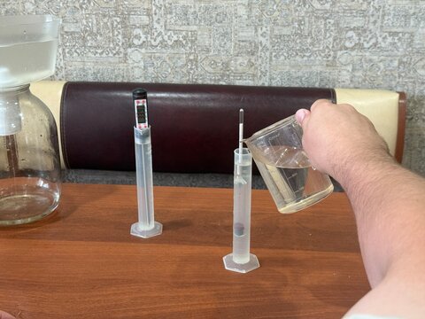 Close up hand of man carefully pouring liquid into graduated cylinder next to digital thermometer and hydrometer preparation of ingredients for crafting homemade alcoholic beverages