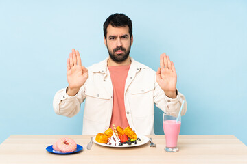 Man at a table having breakfast waffles and a milkshake making stop gesture and disappointed