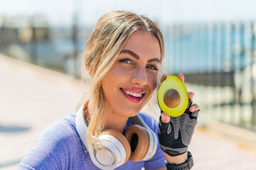 Young pretty sport woman at outdoors holding an avocado with happy expression