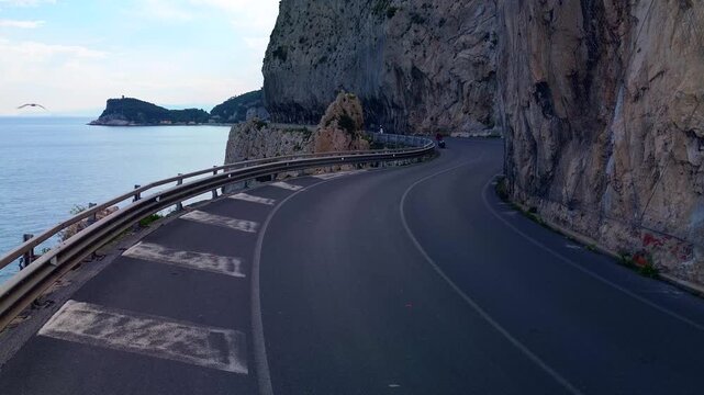 aerial shot. Travel by the sea. Serpentine asphalt road under the cliff. Tourism. Stone Cave of counterfeiters in Capo Noli in Liguria, Italy 19.08.2025