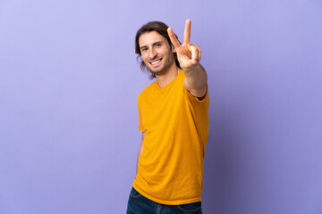 Young handsome man isolated on purple background smiling and showing victory sign