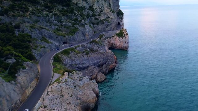 aerial shot. Travel by the sea. Serpentine asphalt road under the cliff. Tourism. Stone Cave of counterfeiters in Capo Noli in Liguria, Italy 19.08.2025