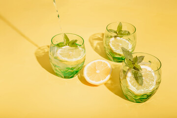 Fresh lemonade in the making: water is being poured into a green glass filled with ice, lemon slices, and mint.