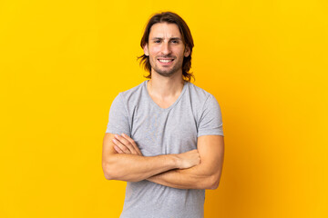 Young handsome man isolated on yellow background keeping the arms crossed in frontal position