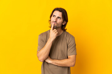 Young handsome man isolated on yellow background having doubts while looking up