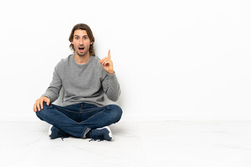 Young handsome man sitting on the floor over isolated background intending to realizes the solution while lifting a finger up