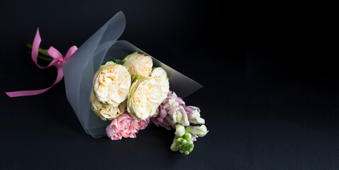 Beautiful small bouquet with pink and white roses on a black background. Copy space. Close-up.