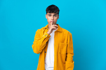 Young man over isolated blue background showing a sign of silence gesture putting finger in mouth