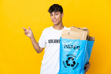 Man holding a recycling bag full of paper to recycle over isolated yellow background pointing...