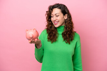 Young caucasian woman holding piggybank isolated on pink background with happy expression