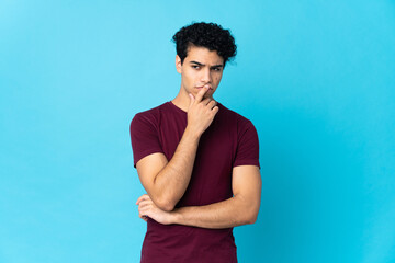 Young Venezuelan man isolated on blue background having doubts while looking up
