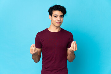 Young Venezuelan man isolated on blue background making money gesture but is ruined