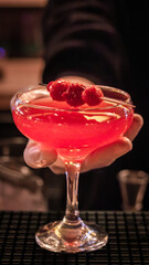 Raspberry cocktail being held over bar counter grid matting.