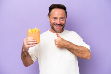Middle age caucasian man holding fried chips isolated on purple bakcground giving a thumbs up...